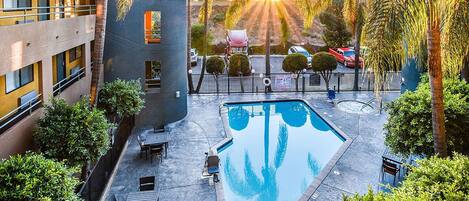A rooftop pool with a view of the sunset, surrounded by palm trees and a building with balconies.
