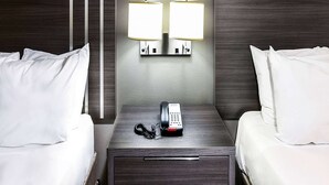 Habitació d'hotel amb un llit, una taula de nit amb telèfon i dues làmpades penjades a la paret.