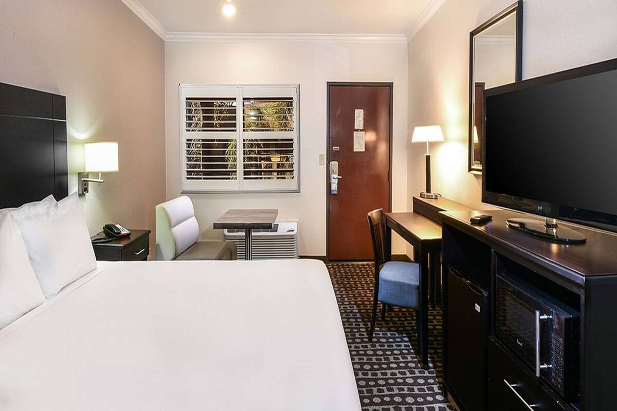 Habitación de hotel con cama, escritorio, silla, televisor y ventana con persianas.