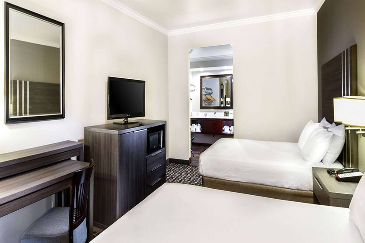 Una habitación de hotel con cama, escritorio con televisor, espejo y armario.