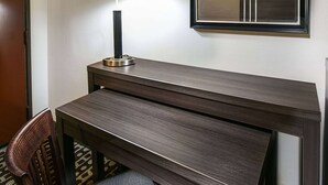 Habitació d'hotel amb escriptori de fusta, una làmpada i un mirall a la paret.