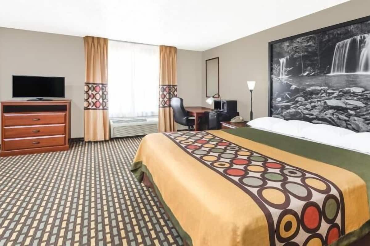 A hotel room with a bed, a television, a desk, a chair, and a large window with curtains.