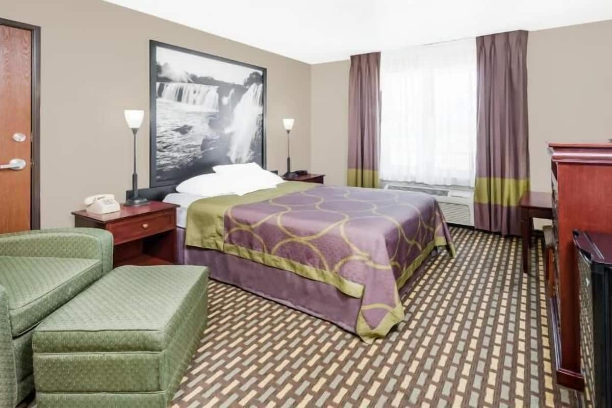 A hotel room with a bed, a desk, a television, a chair, and a large window with curtains.