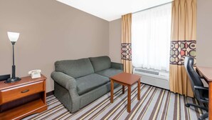 Habitación de hotel con sofá, una pequeña mesa de madera, lámpara, teléfono, silla y ventana con cortinas.