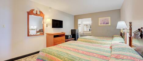A hotel room with two beds, a desk, a mirror, a television, and a lamp.