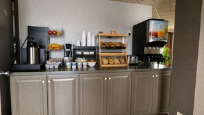 A kitchenette with a coffee machine, fruit bowl, bread display, and a juice dispenser.