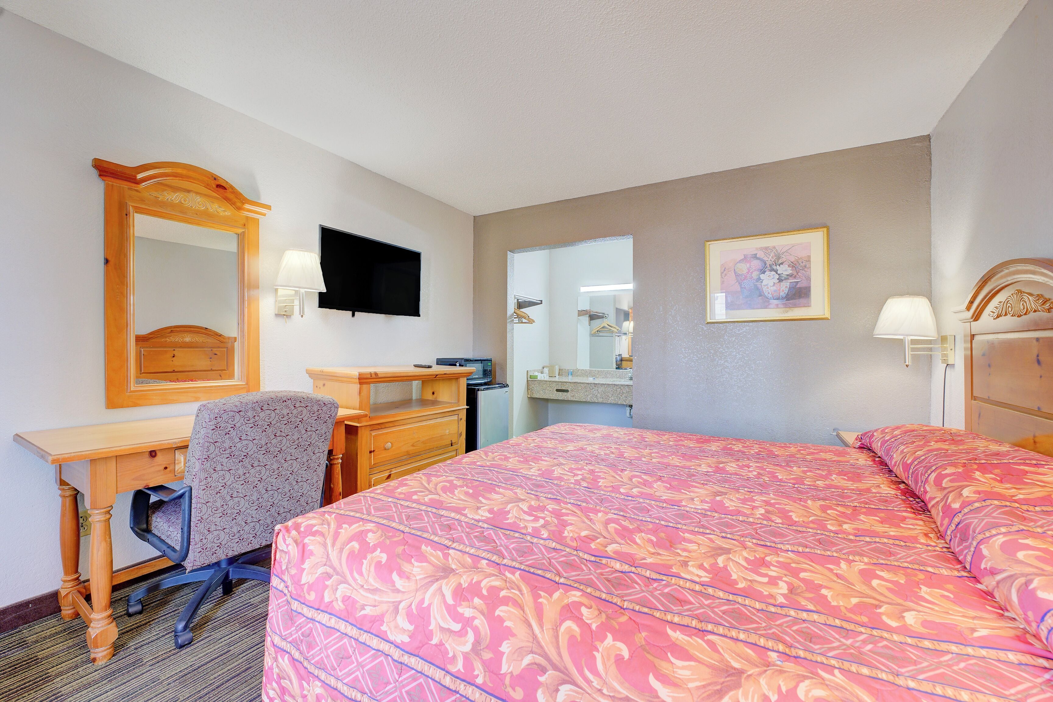 A hotel room with a bed, desk, chair, dresser, and a television.