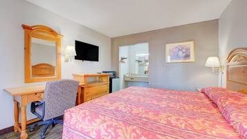 A hotel room with a bed, desk, chair, dresser, and a television.