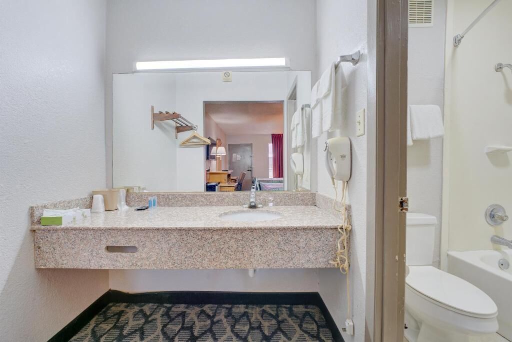 A bathroom with a granite countertop, a sink, a mirror, a towel rack, and a toilet.