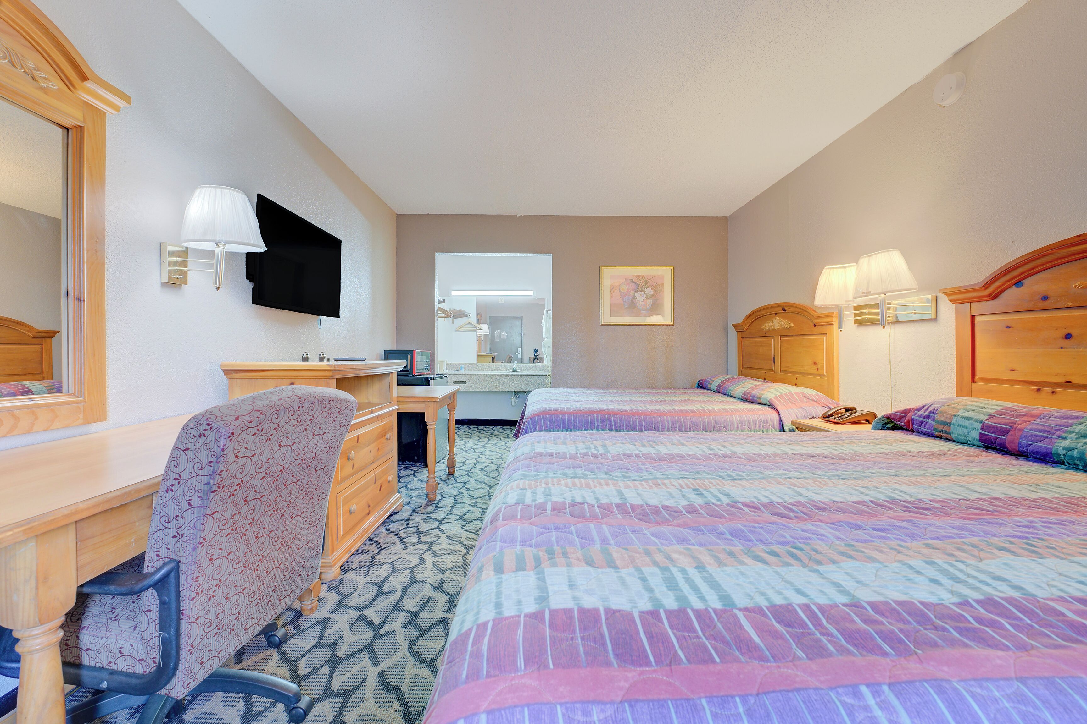 A hotel room with a desk, two beds, a dresser, a mirror, and wall-mounted lamps.