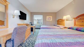 A hotel room with a desk, two beds, a dresser, a mirror, and wall-mounted lamps.