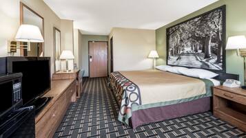 Habitación de hotel con cama, televisor, escritorio, lámpara y un cuadro en la pared.