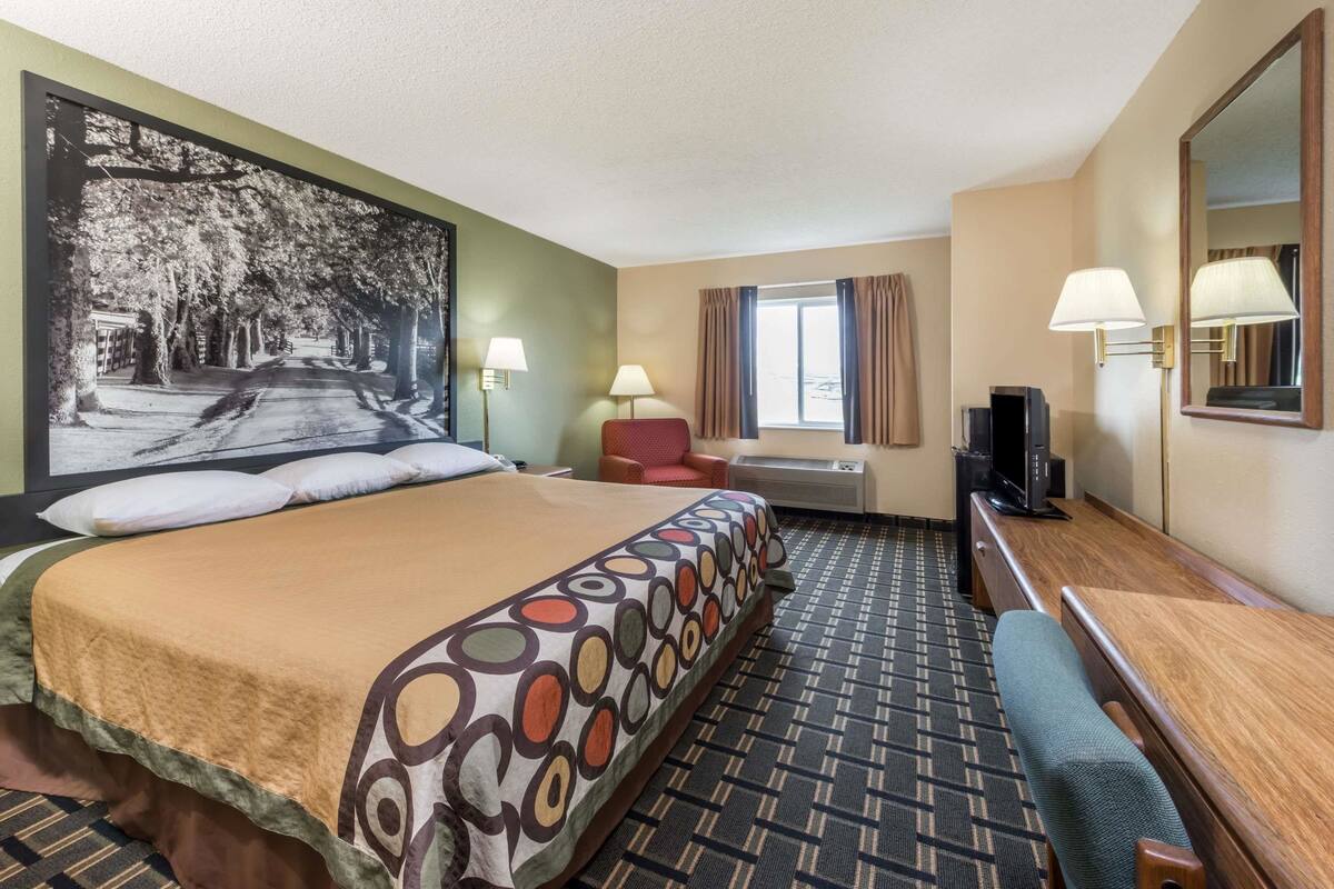 Habitación de hotel con una cama grande, un escritorio, una silla, un televisor y una ventana con cortinas.