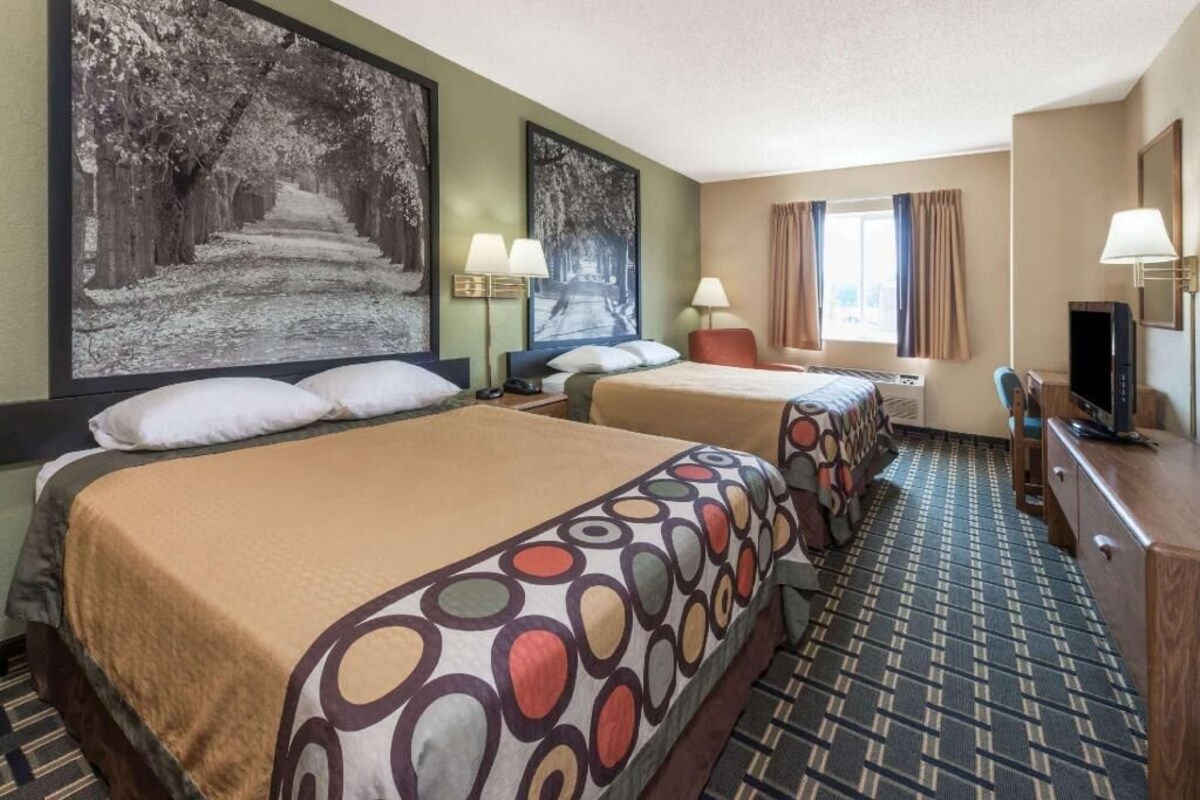 Habitación de hotel con dos camas, un escritorio, un televisor y obras de arte en las paredes.