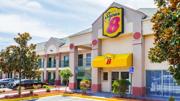 A Super 8 hotel with a yellow awning, a wheelchair-accessible entrance, and a parking lot with cars. - Super 8 by Wyndham Stafford (Stafford)