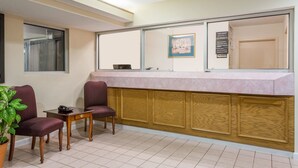 A reception area with a counter, two chairs, a small table, and a potted plant. - Super 8 by Wyndham Stafford (Stafford)