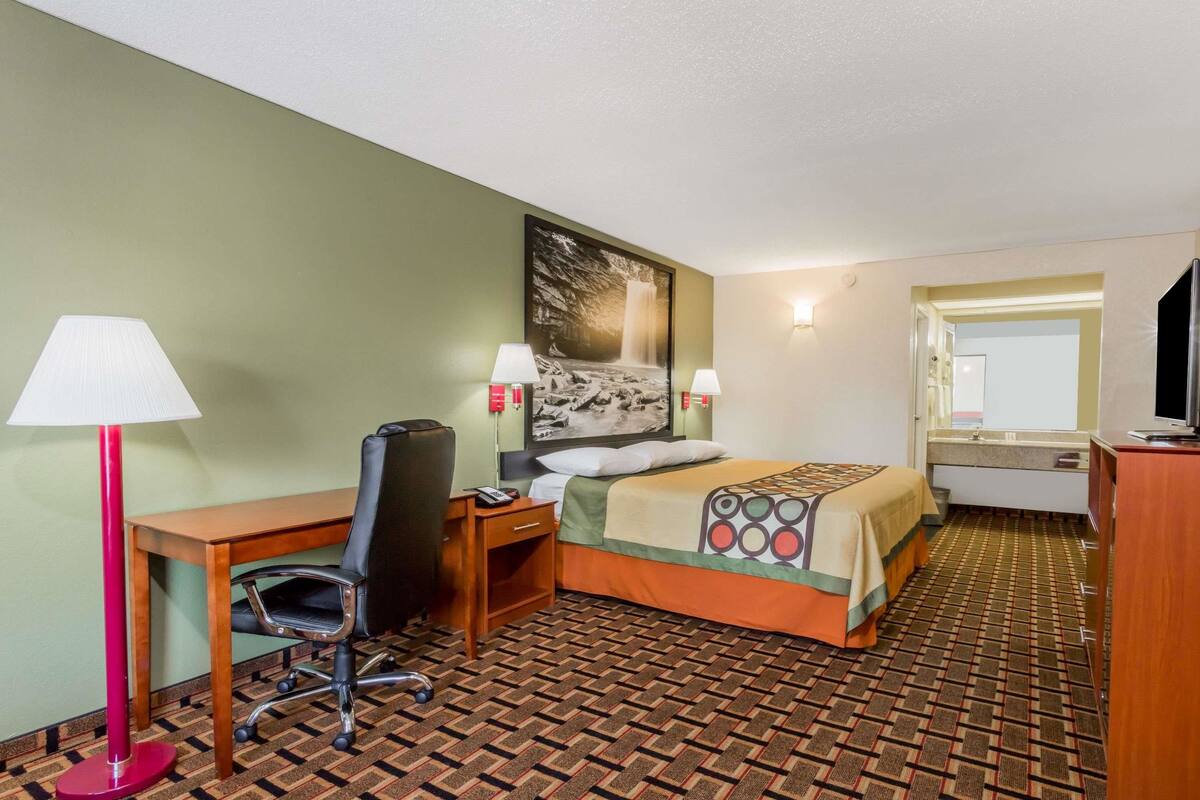 Ein Hotelzimmer mit Bett, Schreibtisch, Stuhl, Lampen und einem Bild an der Wand.