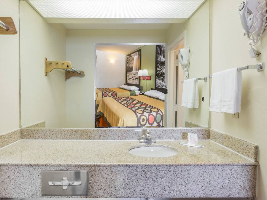 Un baño con encimera de granito, lavabo, espejo y toallero.