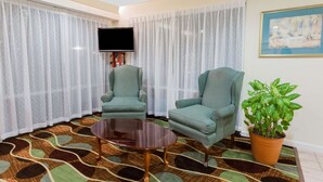 A living room with two green armchairs, a round coffee table, a potted plant, a flat-screen TV, and a patterned carpet. - Super 8 by Wyndham Stafford (Stafford)
