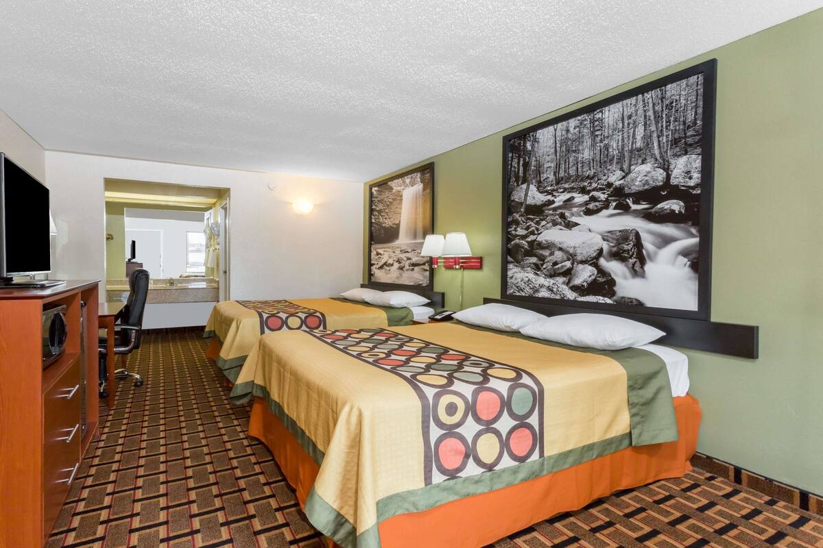 Ein Hotelzimmer mit zwei Betten, einem Schreibtisch, einem Sessel, einem Fernseher und einem großen Bild einer Wasserfall.