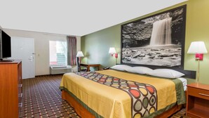 A hotel room with a bed, a desk, a chair, a TV, a window with curtains, and a wall-mounted lamp. - Super 8 by Wyndham Stafford (Stafford)