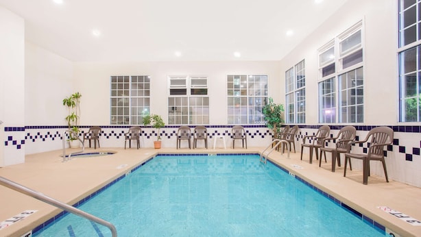 A swimming pool with a tiled border, multiple windows, and several chairs along the poolside. - SureStay Hotel by Best Western North Myrtle Beach (North Myrtle Beach)