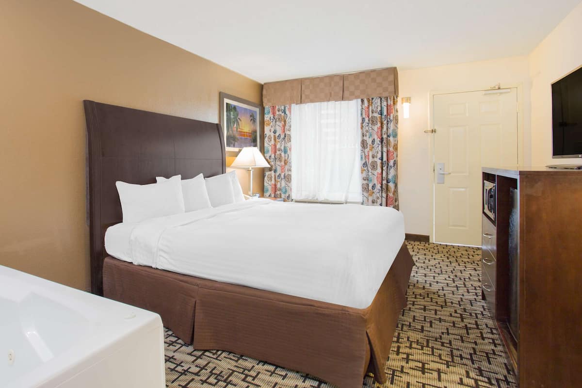 Ein Hotelzimmer mit einem großen Bett, einem Schreibtisch mit Flachbildfernseher, einem Badezimmer mit Badewanne und einem gemusterten Teppich.