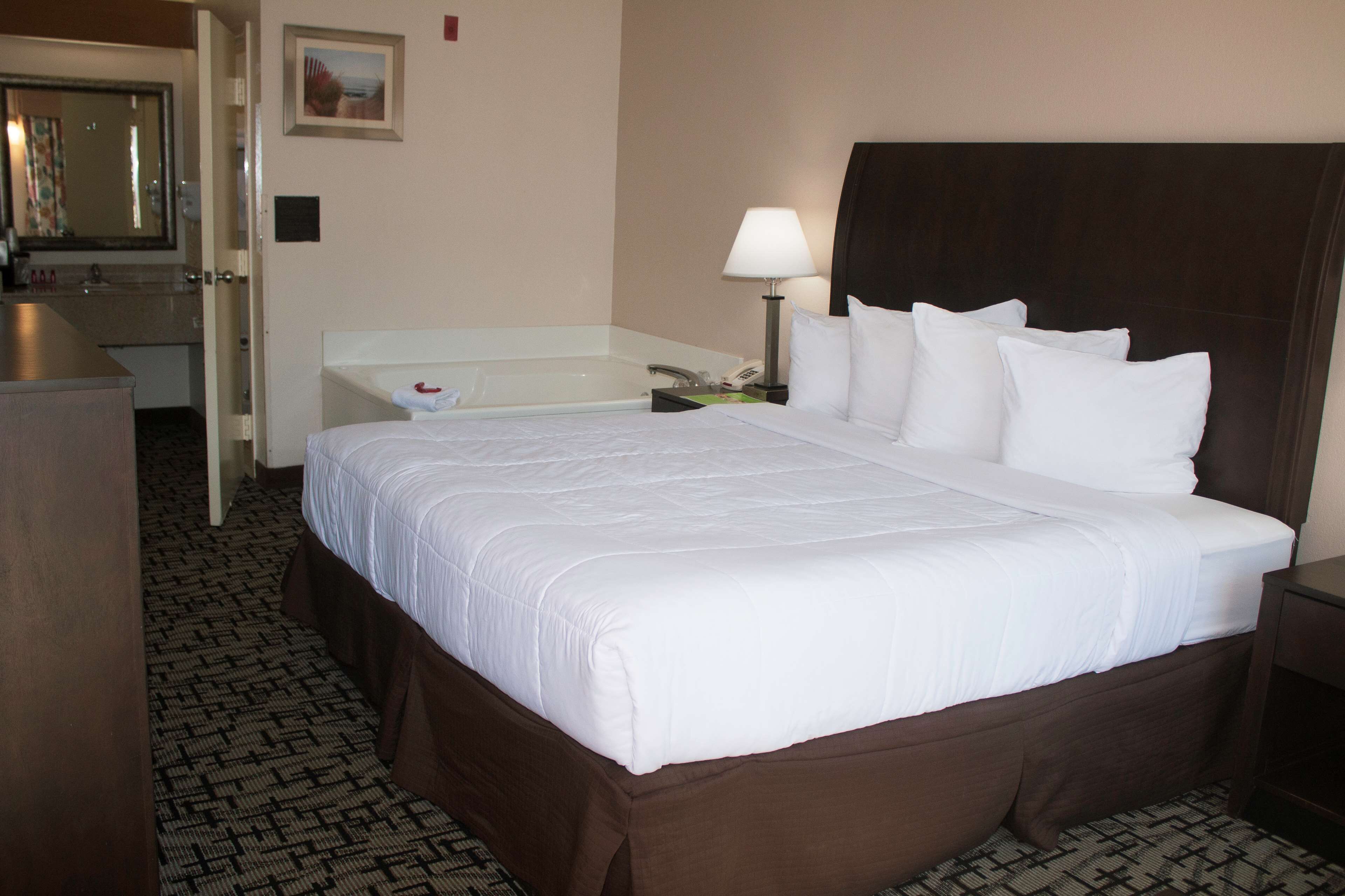 A hotel room with a large bed, a bathroom with a bathtub, and a desk with a lamp.
