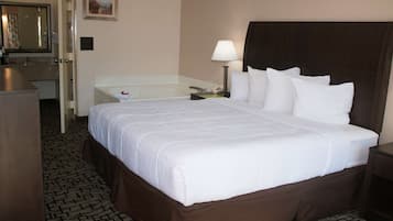 A hotel room with a large bed, a bathroom with a bathtub, and a desk with a lamp.