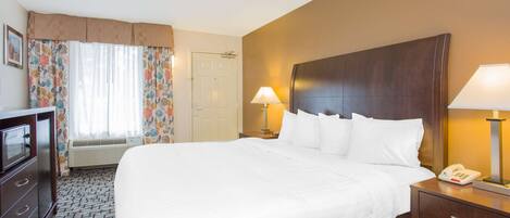 A hotel room with a large bed, two bedside lamps, a telephone, a desk with a lamp, and a television.