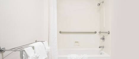 Un baño blanco con ducha, bañera y toallero con toallas.