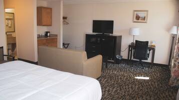 A hotel room with a large bed, a sofa, a television, a desk with a lamp, and a patterned carpet.