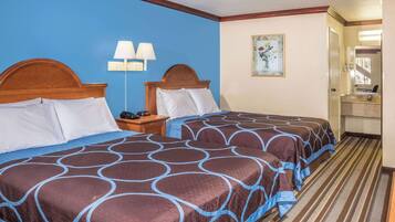 A hotel room with two beds, a nightstand with lamps, a painting on the wall, and a bathroom visible through an open door.