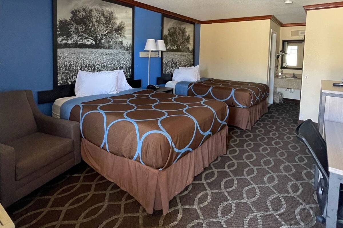 Ein Hotelzimmer mit zwei Betten, einem Schreibtisch, einem Stuhl und einem im Hintergrund erkennbaren Badezimmer.