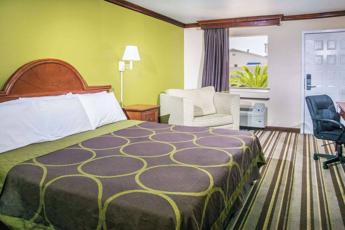 Ein Hotelzimmer mit Bett, Stuhl, Schreibtisch und einem Fenster mit Vorhängen.