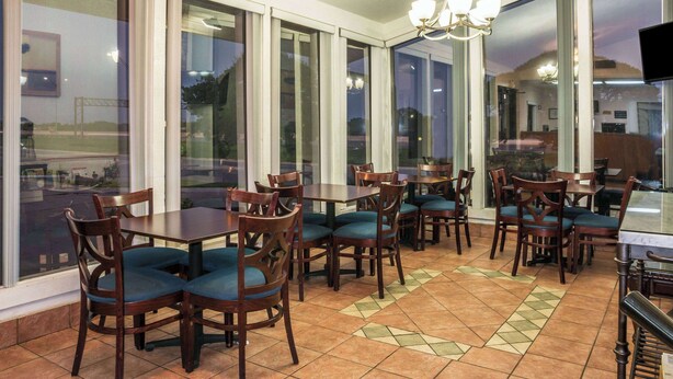 Een restaurant met grote ramen, houten tafels en stoelen met blauwe kussens.