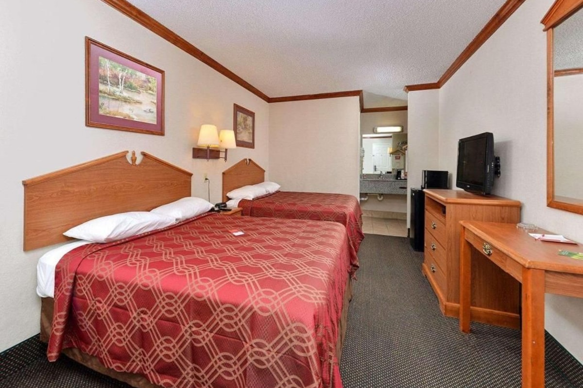 A hotel room with two beds, a desk, a television, and a bathroom visible in the background.