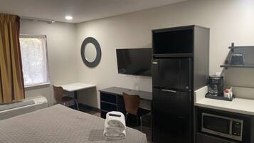 Habitación de hotel con cama, escritorio, silla, televisor, refrigerador, microondas y cafetera.