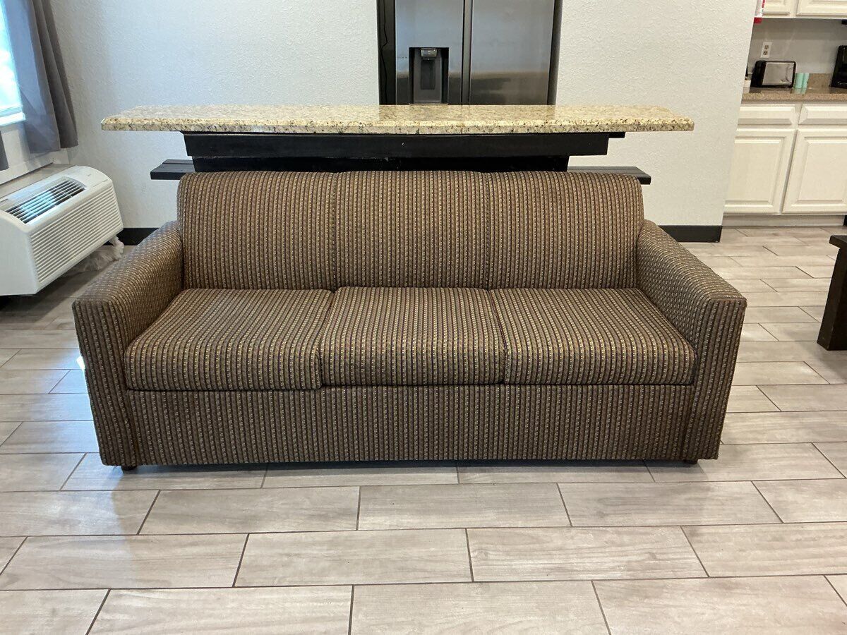 A brown sofa with a patterned fabric, a granite countertop, and a stainless steel refrigerator in the background.