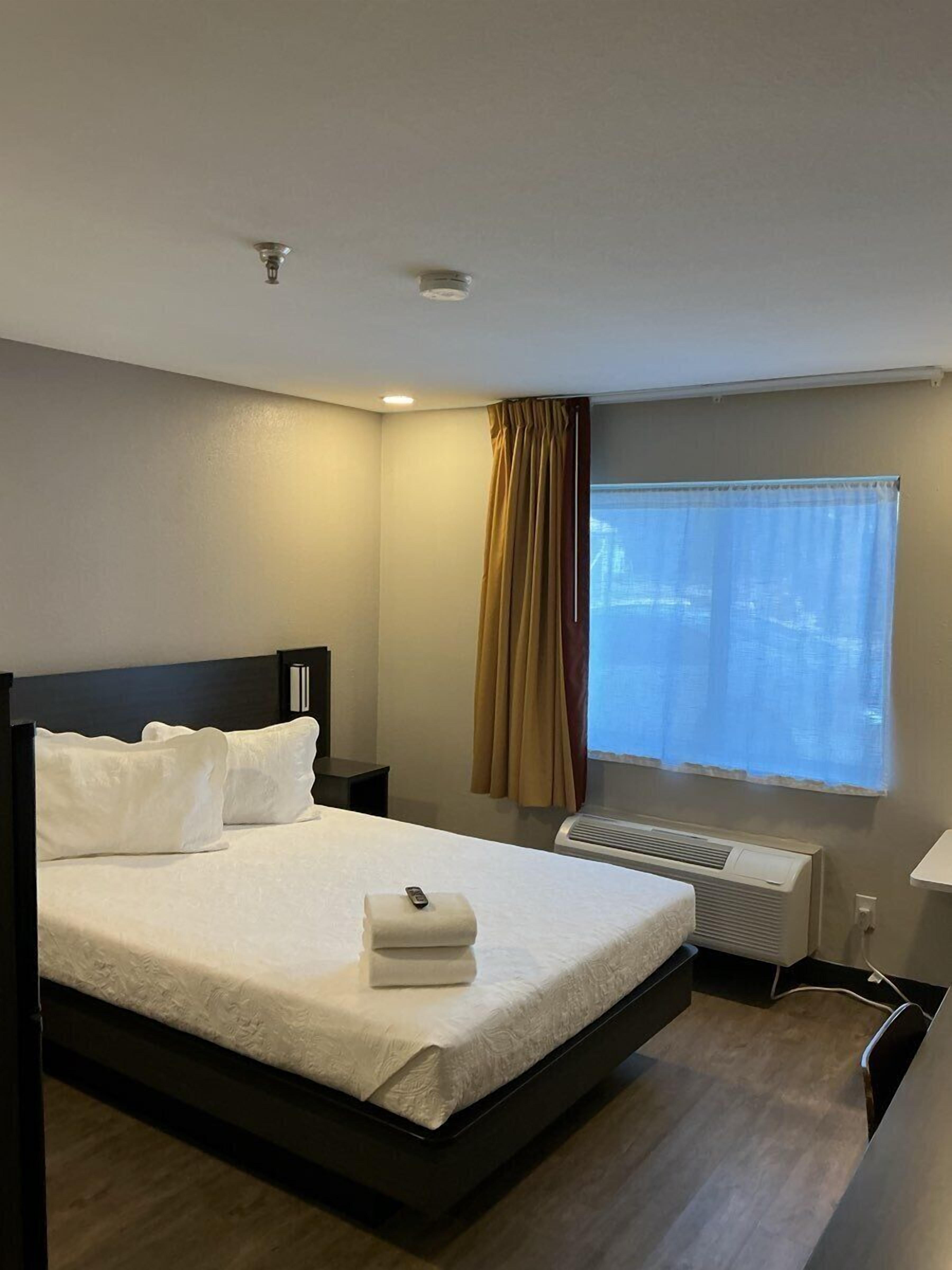 Une chambre d’hôtel comprenant un lit, une table de chevet, une fenêtre avec des rideaux et un climatiseur fixé au mur.