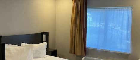 Une chambre d’hôtel comprenant un lit, une table de chevet, une fenêtre avec des rideaux et un climatiseur fixé au mur.