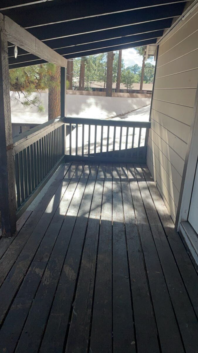 A wooden porch with a railing, a concrete pillar, and a view of a parking area.