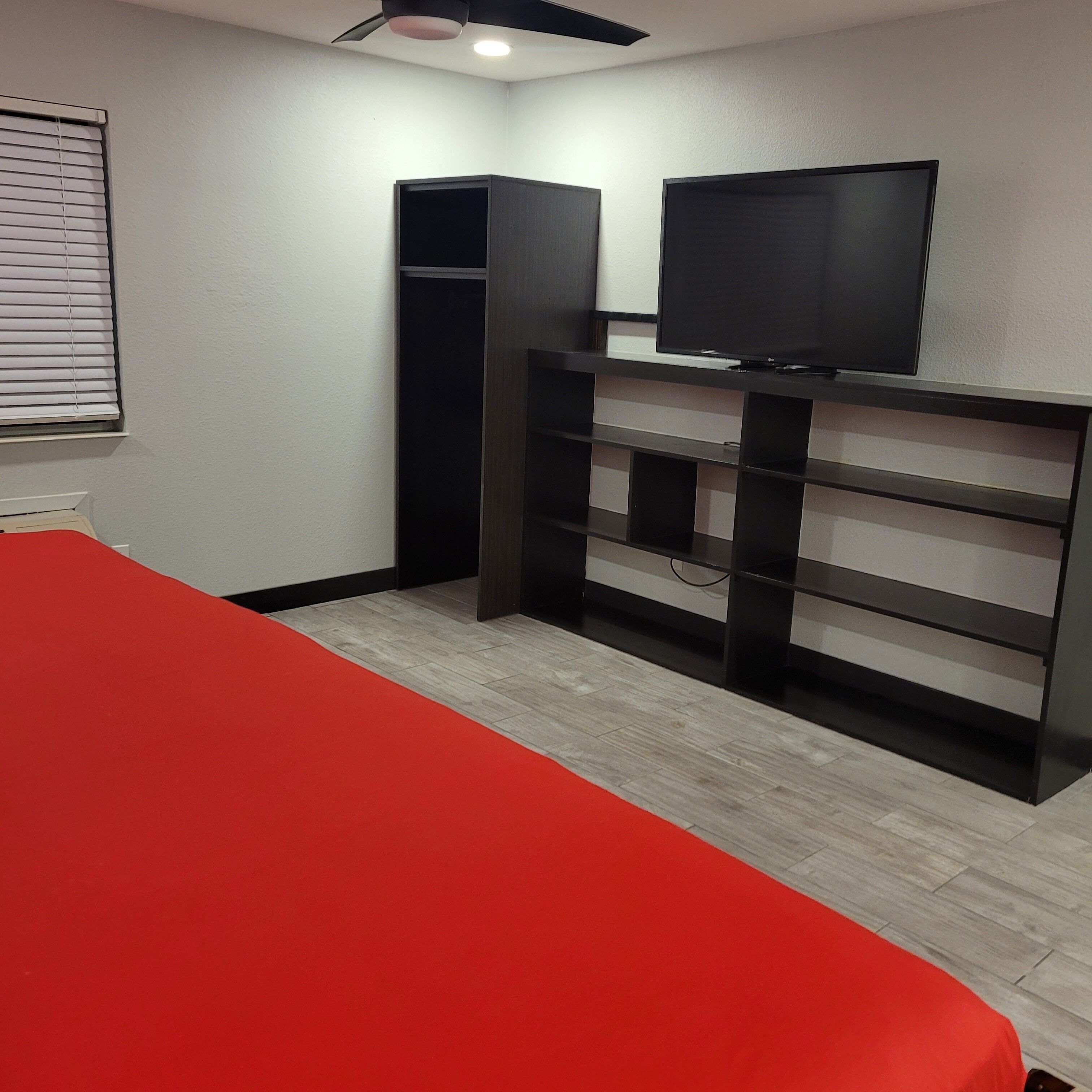 A bedroom with a red bedspread, a black TV stand, and a wardrobe.