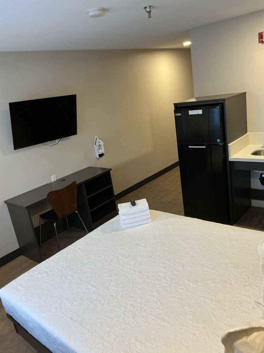 A hotel room with a bed, a desk, a chair, a television, a refrigerator, and a sink.