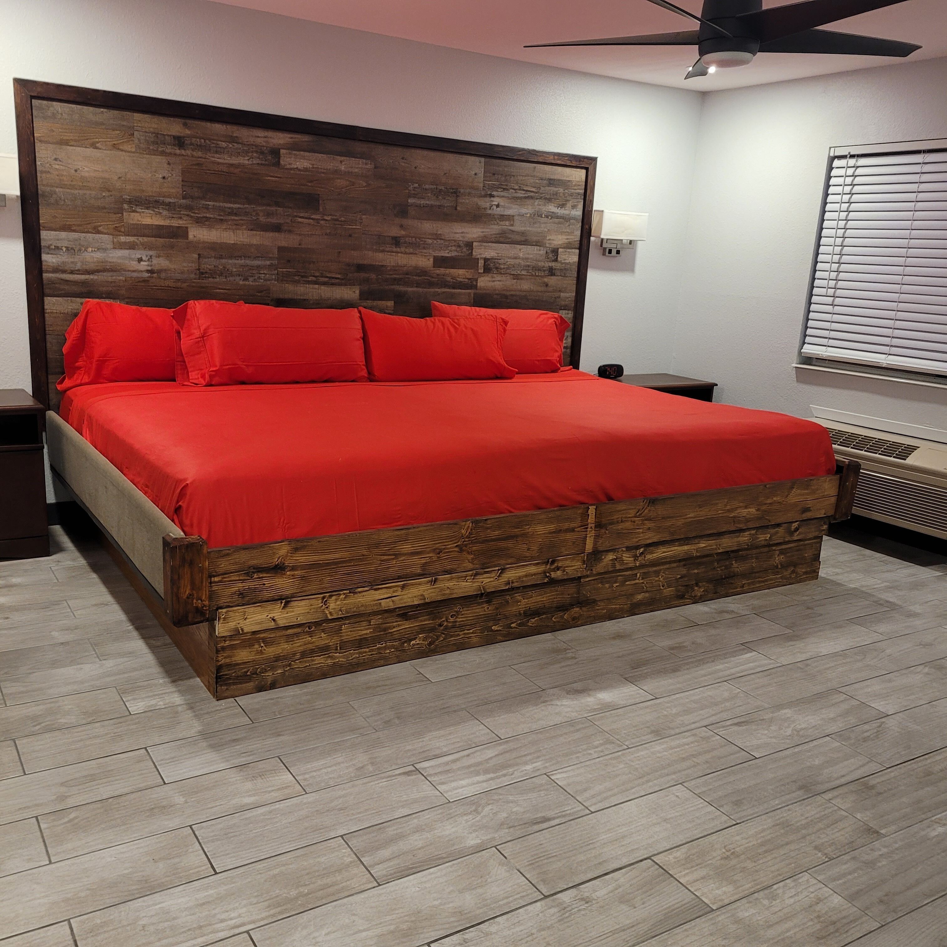 A bed with a wooden headboard, red bedding, and a grey upholstered headboard.
