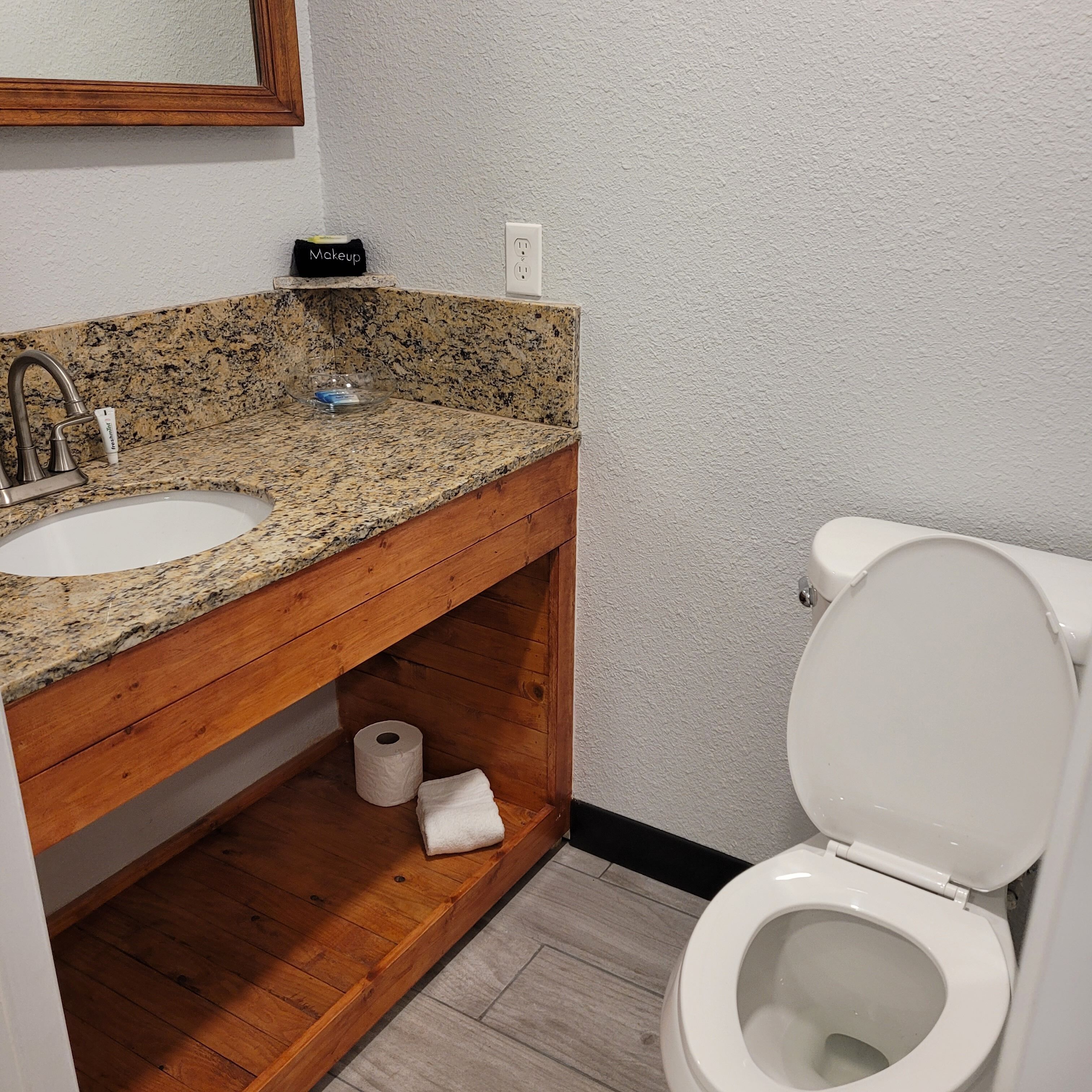 Ein Badezimmer mit Granitwaschtisch, Holzwaschtischunterbau und Toilette.