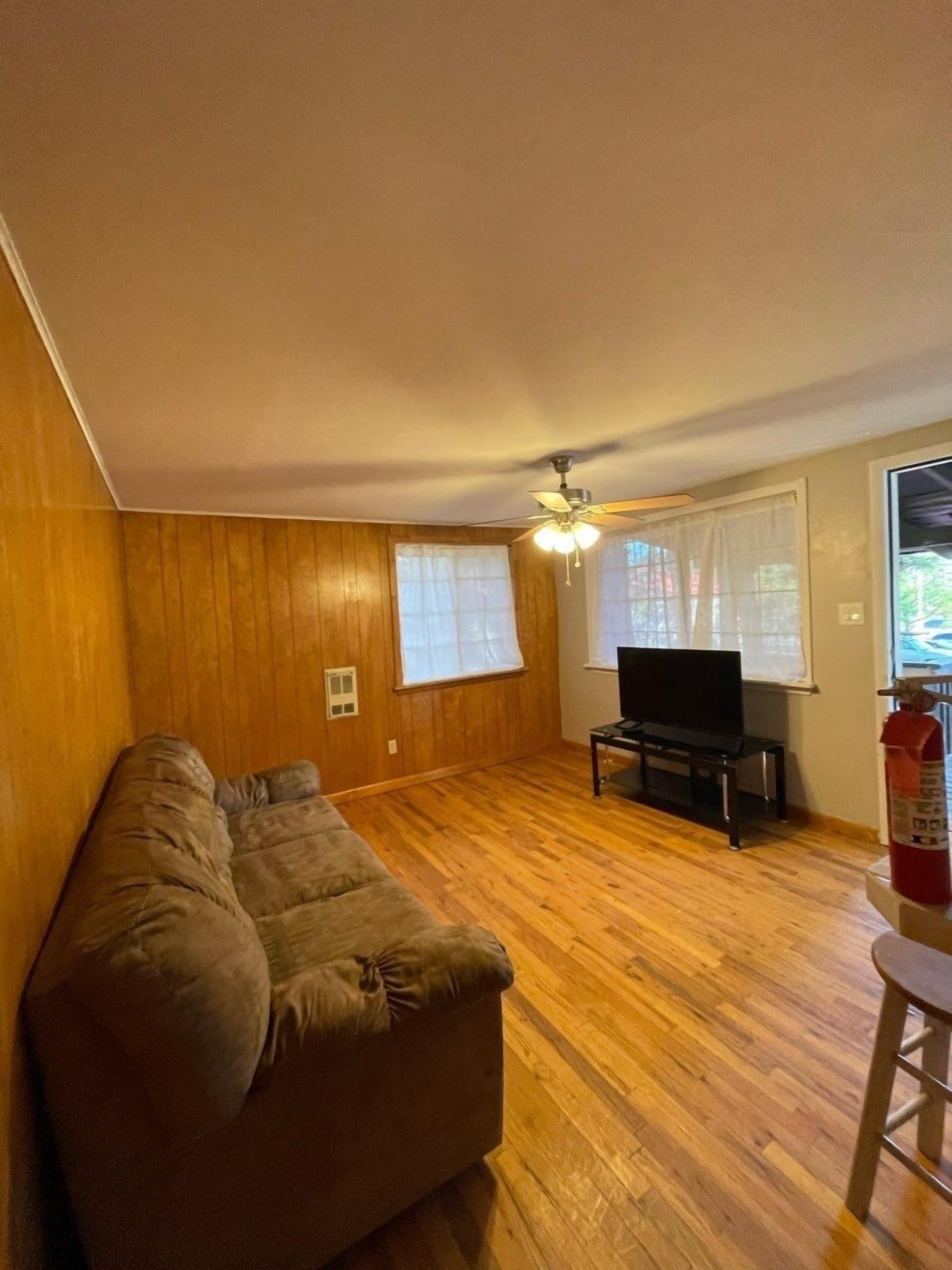 A living room with wooden floors, a sofa, a television, and a ceiling fan.