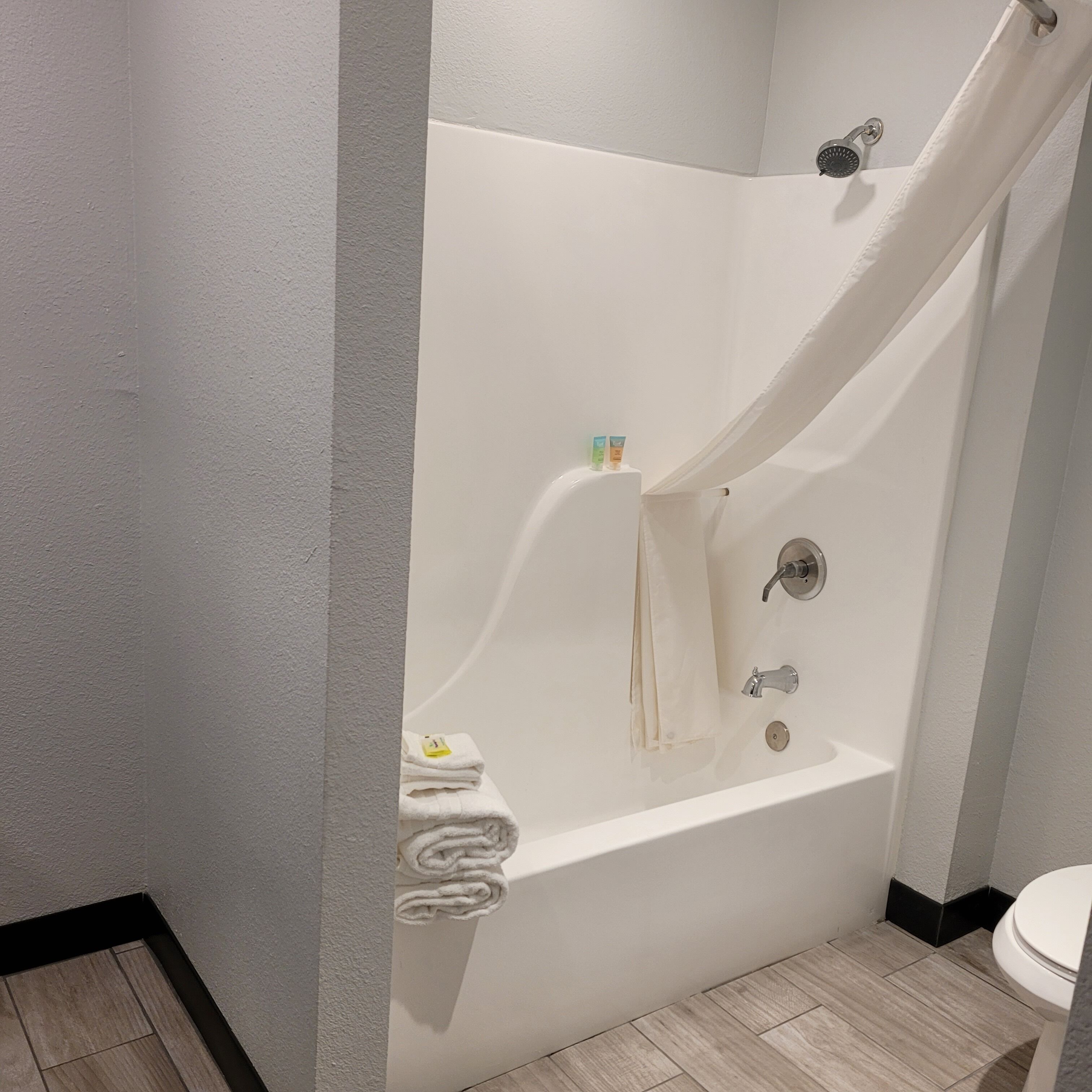 A modern bathroom with a white bathtub, a shower curtain, and a toilet.