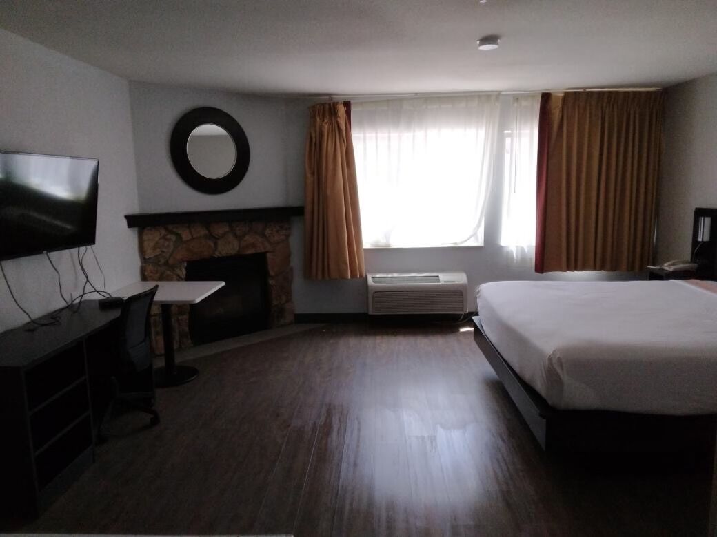 A hotel room with a bed, a TV, a fireplace, and a desk.