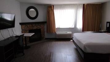 A hotel room with a bed, a TV, a fireplace, and a desk.